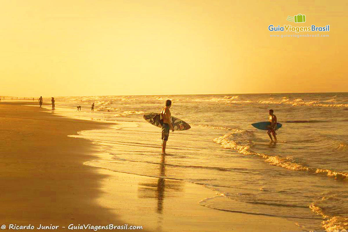 Imagem de surfistas no fim de tarde, na beira da praia em Porto das Dunas.